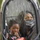 Dana Clarke, wearing an "I can't breathe" mask, holds her son inside a clear protective suit as she waits to vote early.
